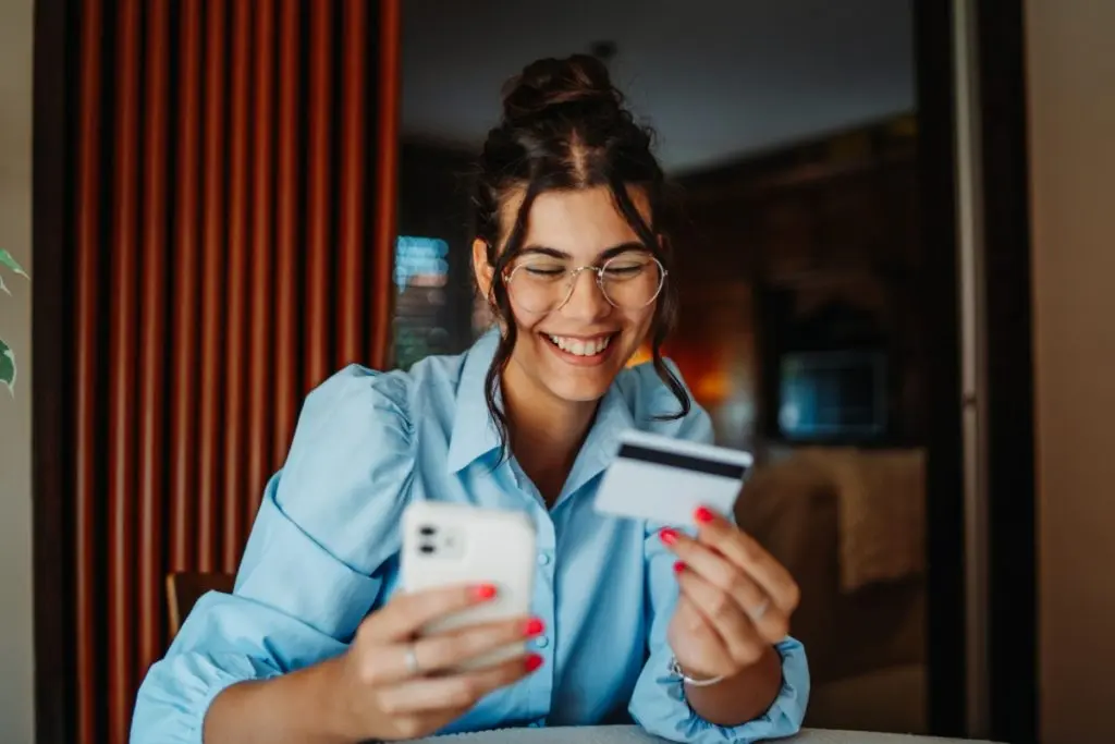 Smiling woman holding phone and credit card in her hands 