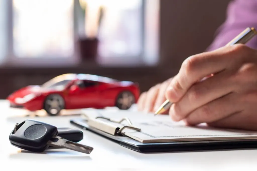 A person signing documents with a car key and a toy car on the table, representing cosigner car loan