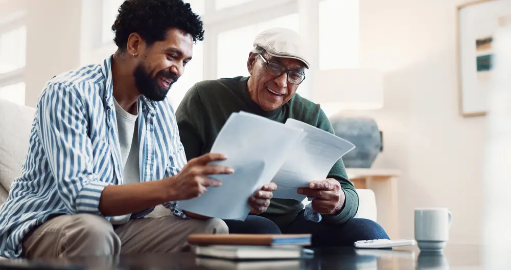 Father and adult son reviewing financial paperwork together on a sofa