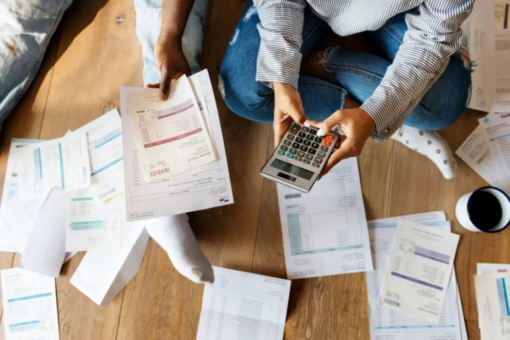 man with calculator sitting on the floor surronded be the invoices papers