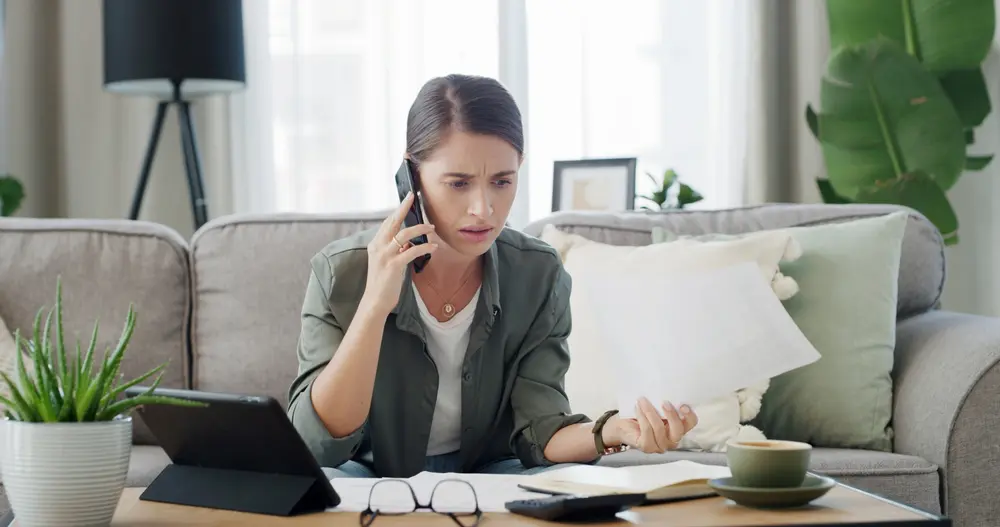 Woman making a phone call while reviewing financial paperwork at home
