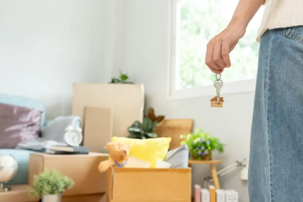 standing woman holding keys from the apartment, in from of the box with the clothes