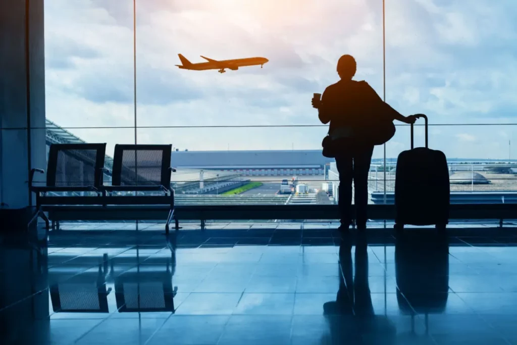 man standing in airport looking at a plane fly